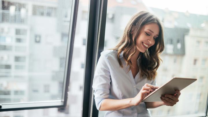 Office person standing by a window looking at a tablet computer